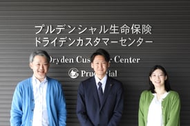 プルデンシャル生命保険株式会社ドライデンカスタマーセンター 総務チームの 渡邉様（左）・山内様（中央）・木曽様（右）が笑顔でプルデンシャル生命保険株式会社のロゴの前に立つ写真