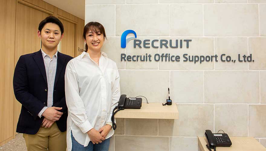 リクルートオフィスサポート株式会社の企業ロゴの横で笑顔で立つ人事部の中島さまと三橋さまの写真
